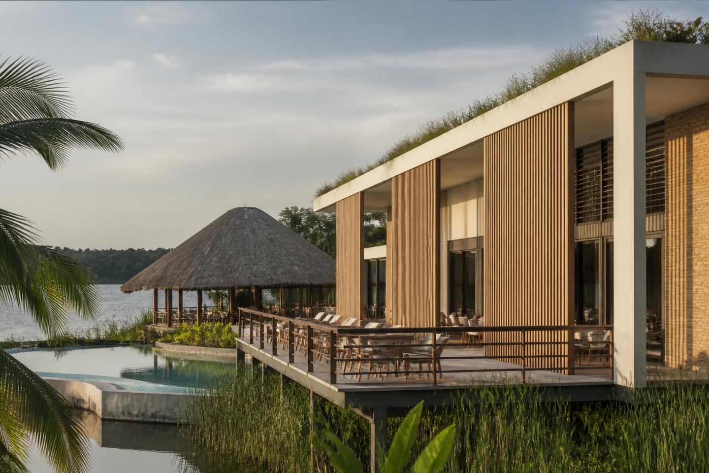 Éco-hôtel contemporain au bord du lac : enduit clair, brise-soleil en bois, toiture végétalisée et pavillon en paille